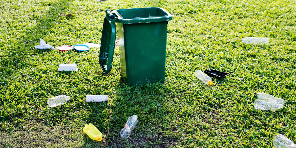 Green outdoor bin with its lid open and empty plastic water bottles scattered on grass