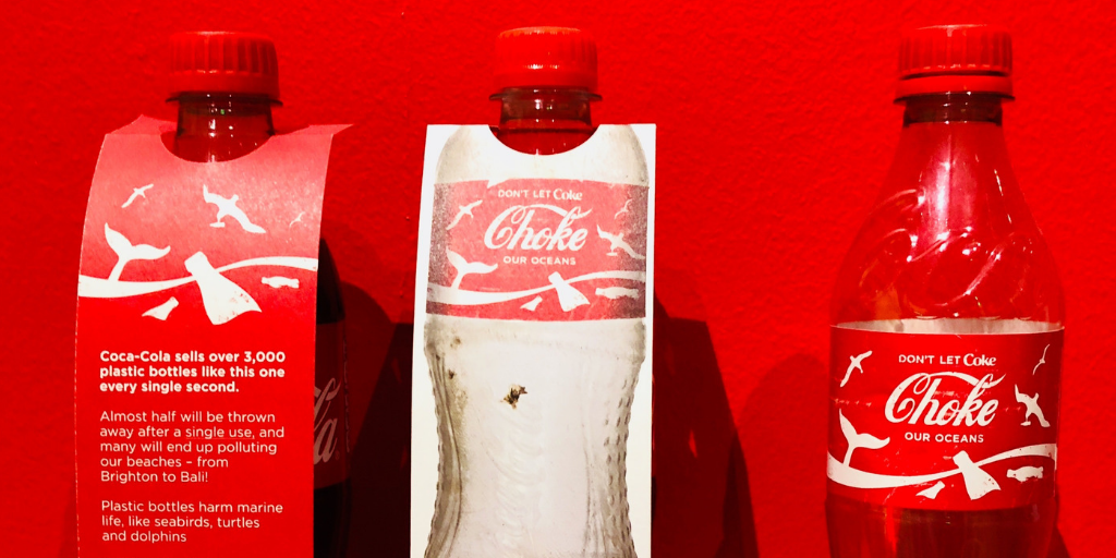 Three red plastic bottles labeled Don't let Coke choke our oceans with a label noting 3,000 bottles sold every second