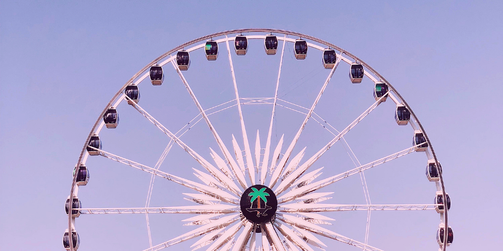 Ferris wheel against a lavender sky at a music festival, central hub showing a green palm logo