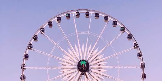 Ferris wheel against a lavender sky at a music festival, central hub showing a green palm logo
