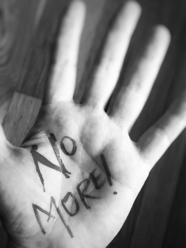 Open hand with 'NO MORE!' written in marker across the palm against a wooden background