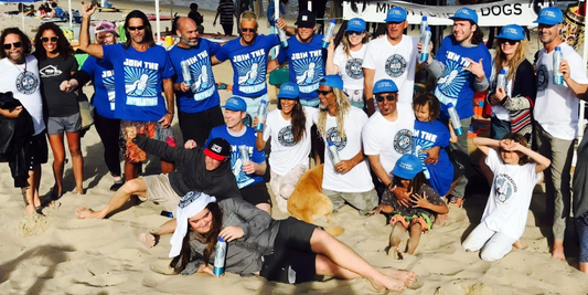 Volunteers posing on a beach after a cleanup, many in blue shirts saying JOIN THE REVOLUTION and holding PATHWATER bottles