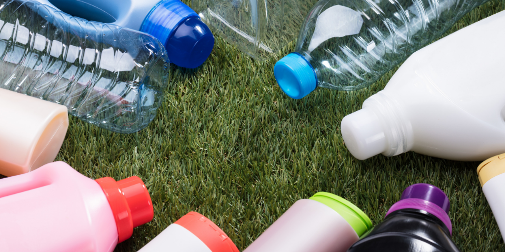 Assortment of empty clear water bottles and colorful detergent jugs scattered on grass