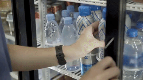 Hand removes a PATH Water reusable aluminum bottle from a refrigerated shelf stocked with plastic water bottles
