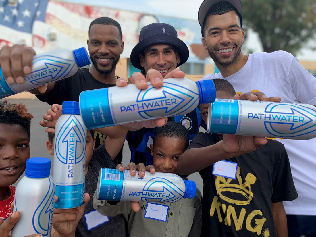 Smiling adults and children holding PATHWATER aluminum water bottles toward the camera in an outdoor community setting