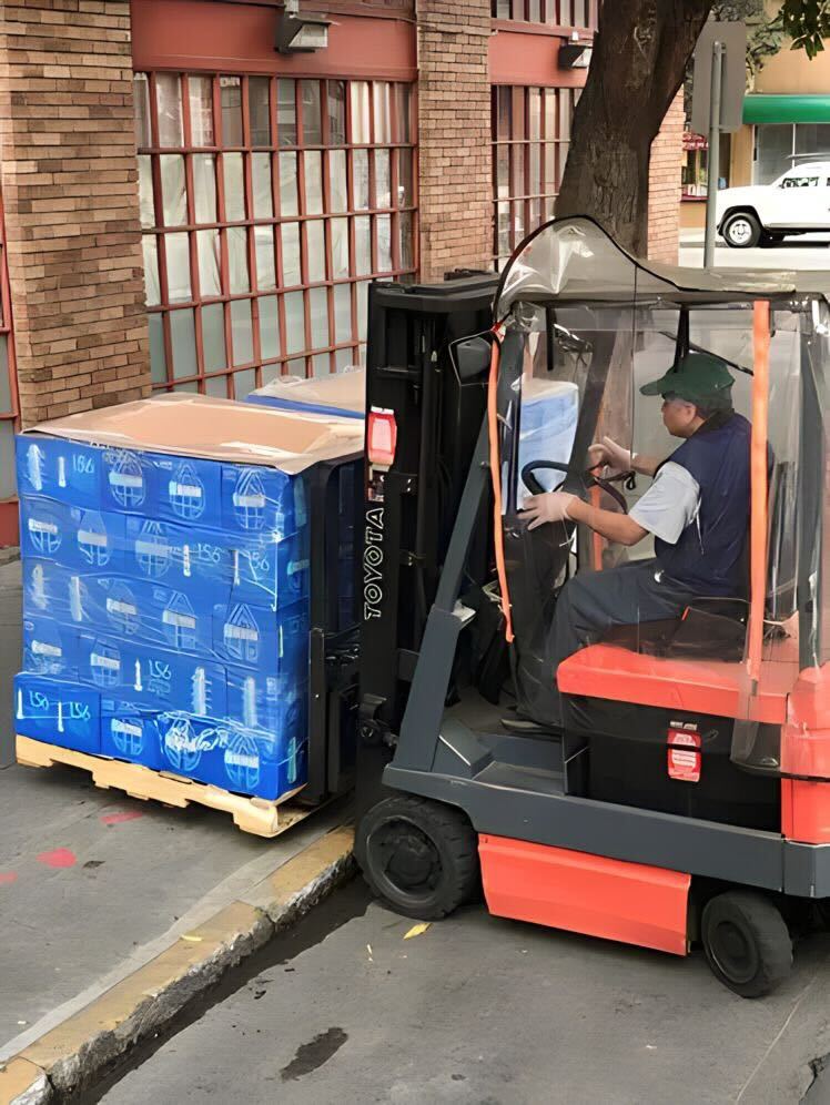 Forklift operator loading a pallet of bottled water outside a brick storefront