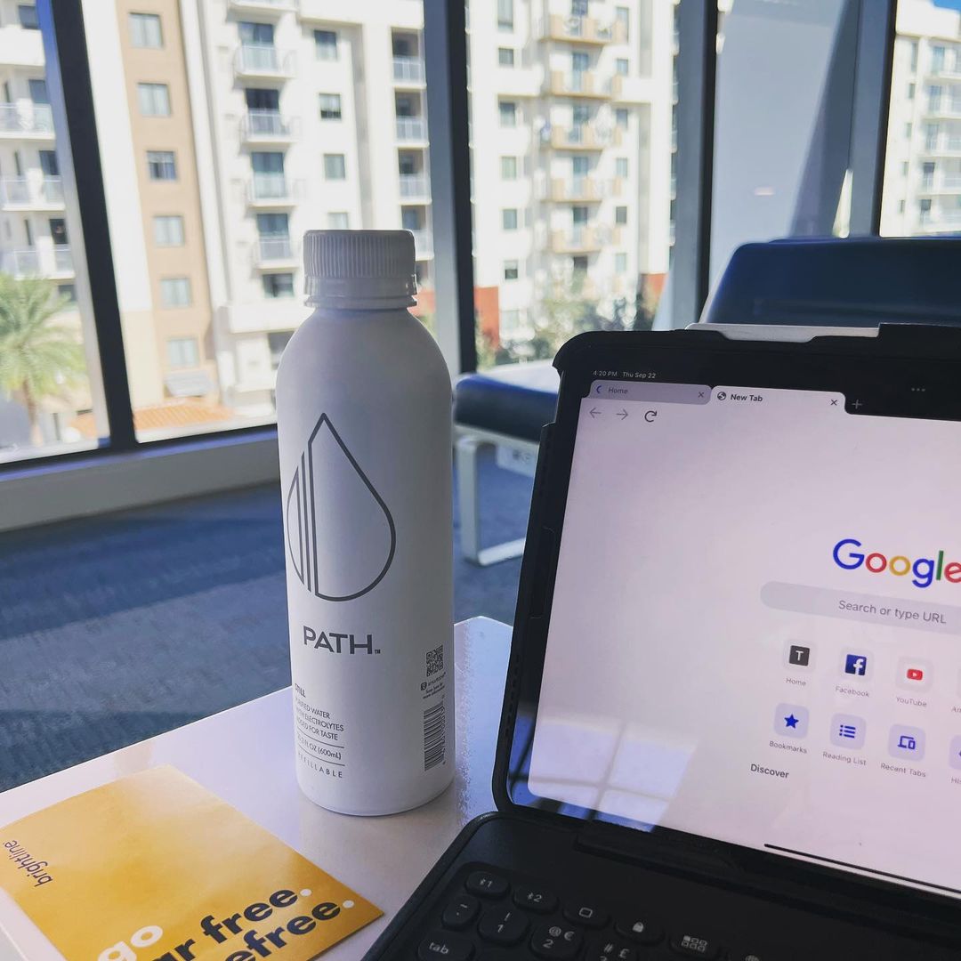 PATH water bottle on a table beside a tablet showing a browser with the Google homepage, apartment windows in the background