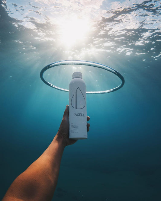 Front view of PATH aluminum bottle showcasing matte white finish and logo with hand holding it underwater toward sunlit surface