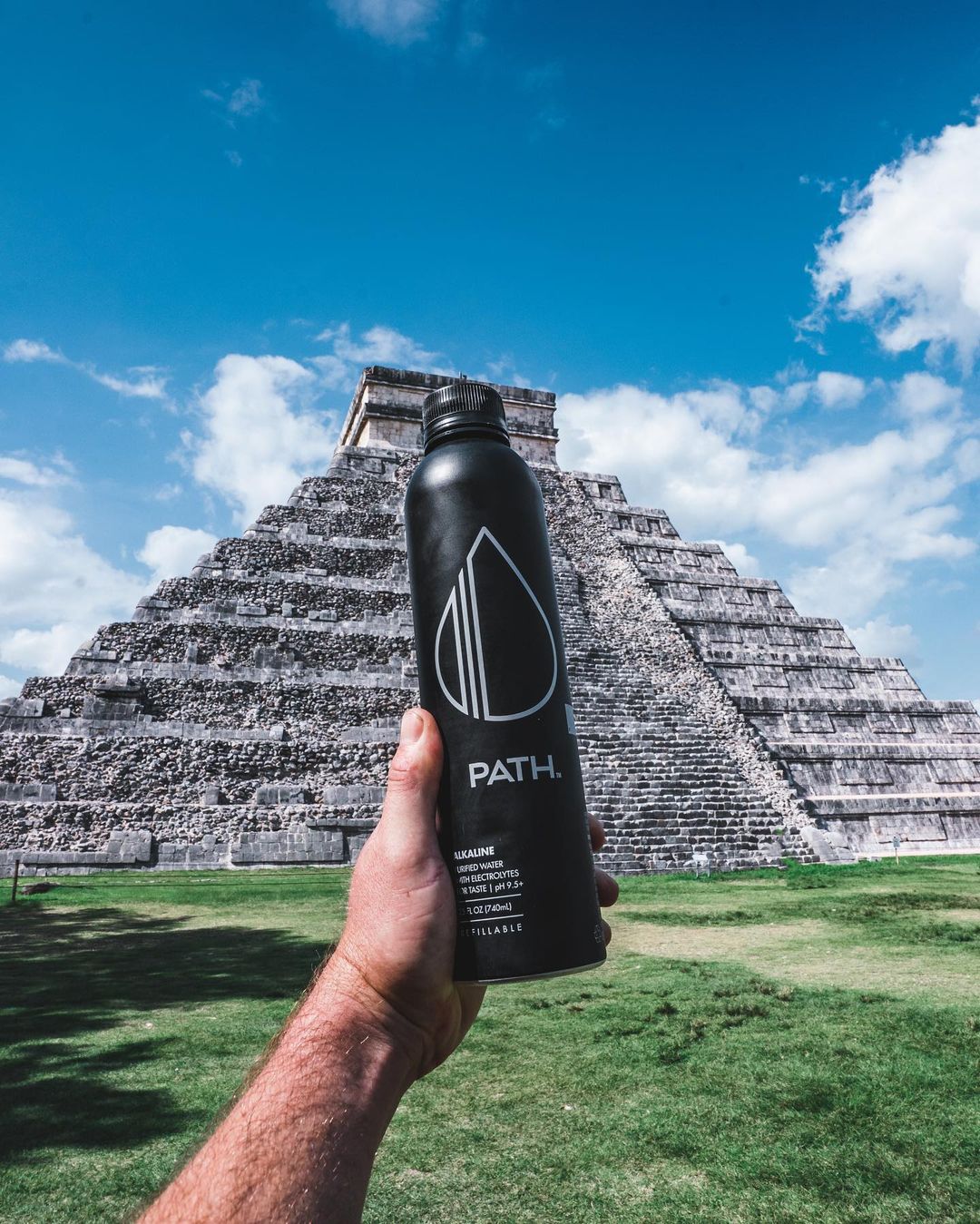 Front view of PATH aluminum water bottle held by hand showing logo and matte black finish with stone pyramid and blue sky