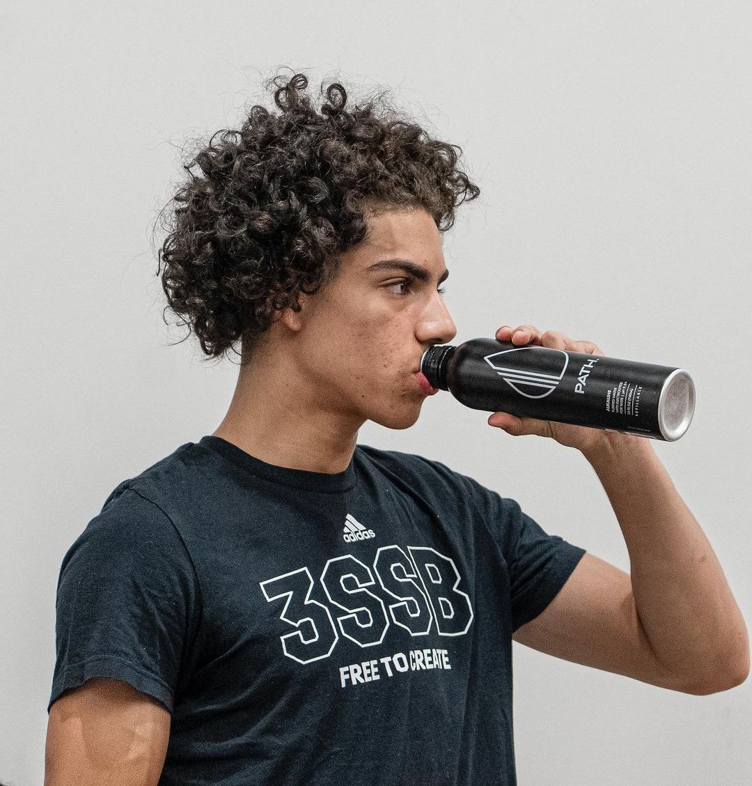 Young man drinking from a black PATH aluminum water bottle against a plain light-gray background