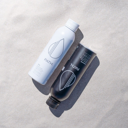 Angled top-down view of white and black PATH aluminum water bottles showing logo and caps on sand