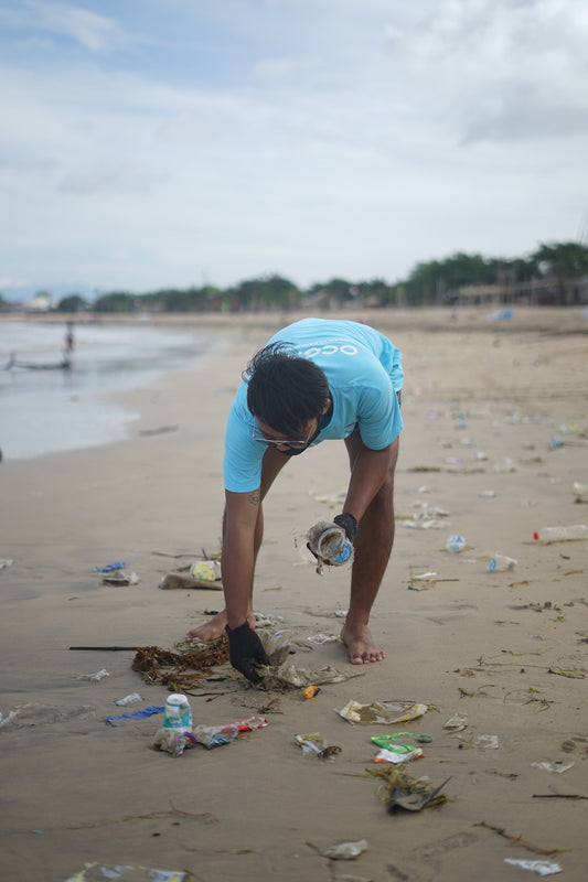 Volunteer picking up plastic bottled water and other trash on a littered beach during a cleanup