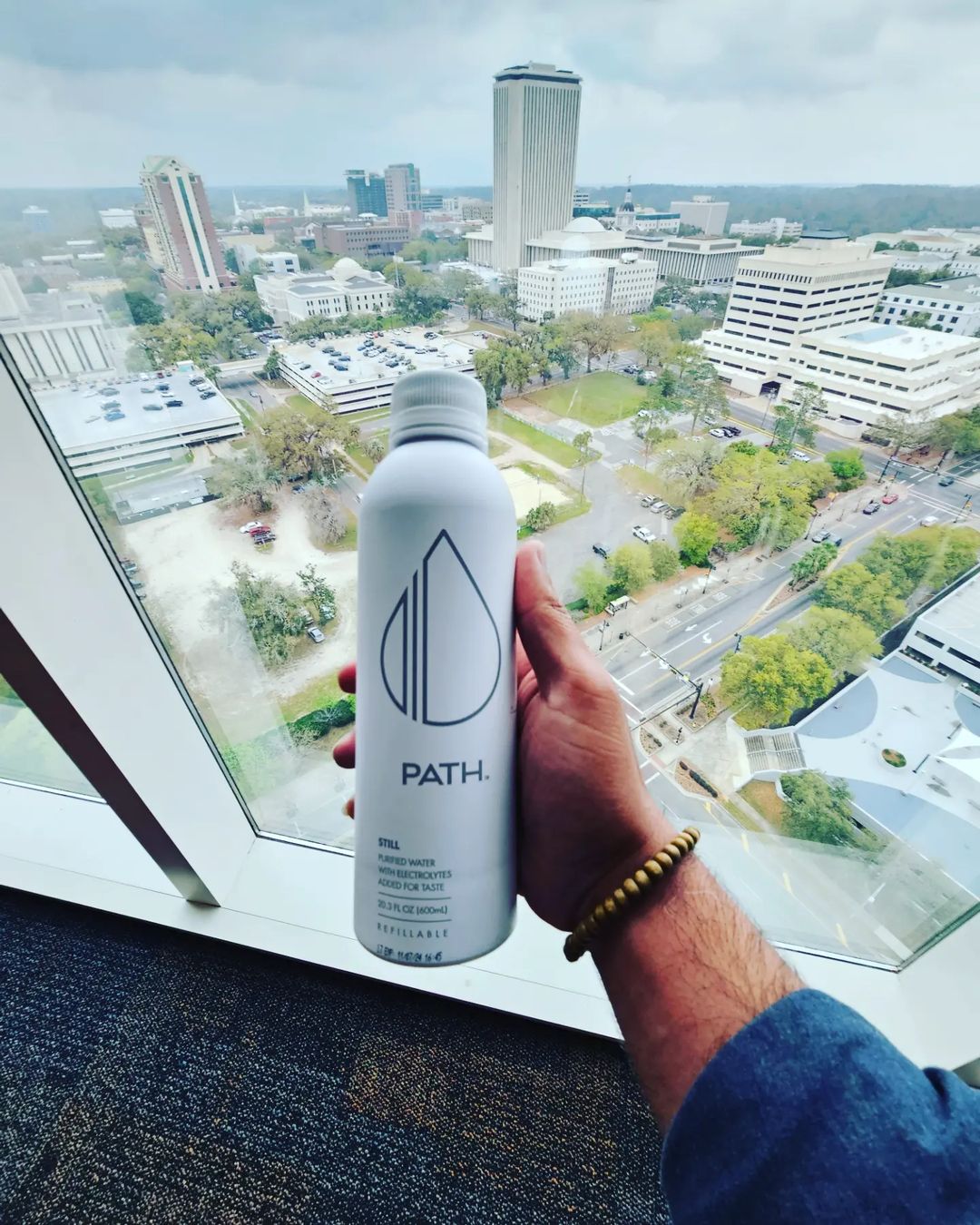 Front view of PATH refillable aluminum water bottle held by hand showing PATH logo and 20.3 fl oz text against a city skyline