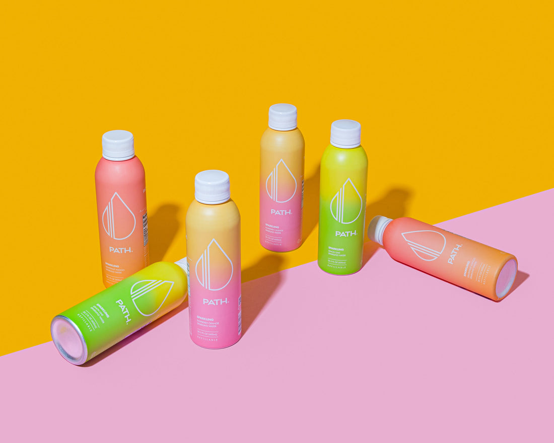 Angled view of six PATH sparkling water bottles with colorful gradient labels on pink-and-yellow background