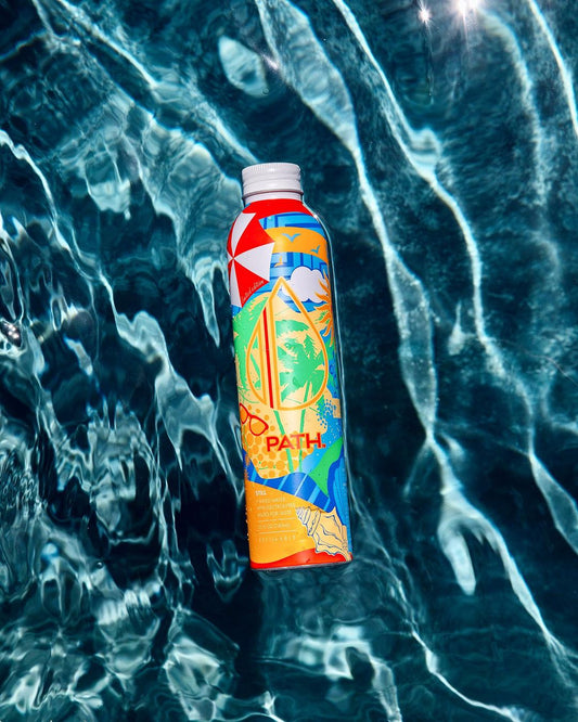 Front view of PATH water bottle showcasing colorful tropical graphic design floating on rippling pool water