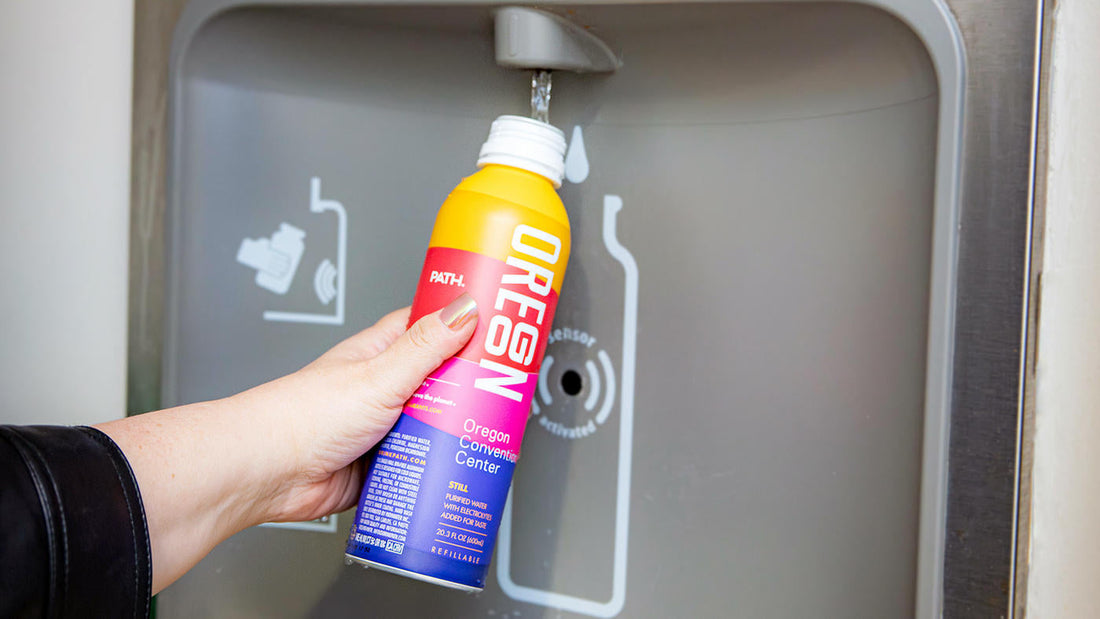 Hand holding a PATH Oregon refillable water bottle under an automatic stainless-steel refill station spout