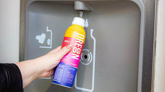 Hand holding a PATH Oregon refillable water bottle under an automatic stainless-steel refill station spout