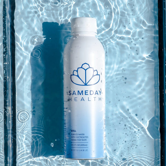 Top-down view of SameDay Health aluminum bottled water showcasing blue lotus logo and label with rippling pool water background