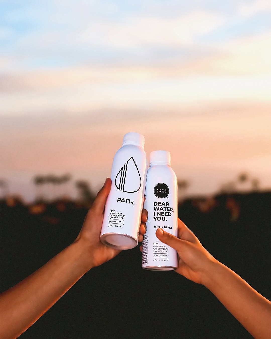 Two PATH aluminum water bottles held together in a toast at sunset, one labeled "Dear water, I need you"