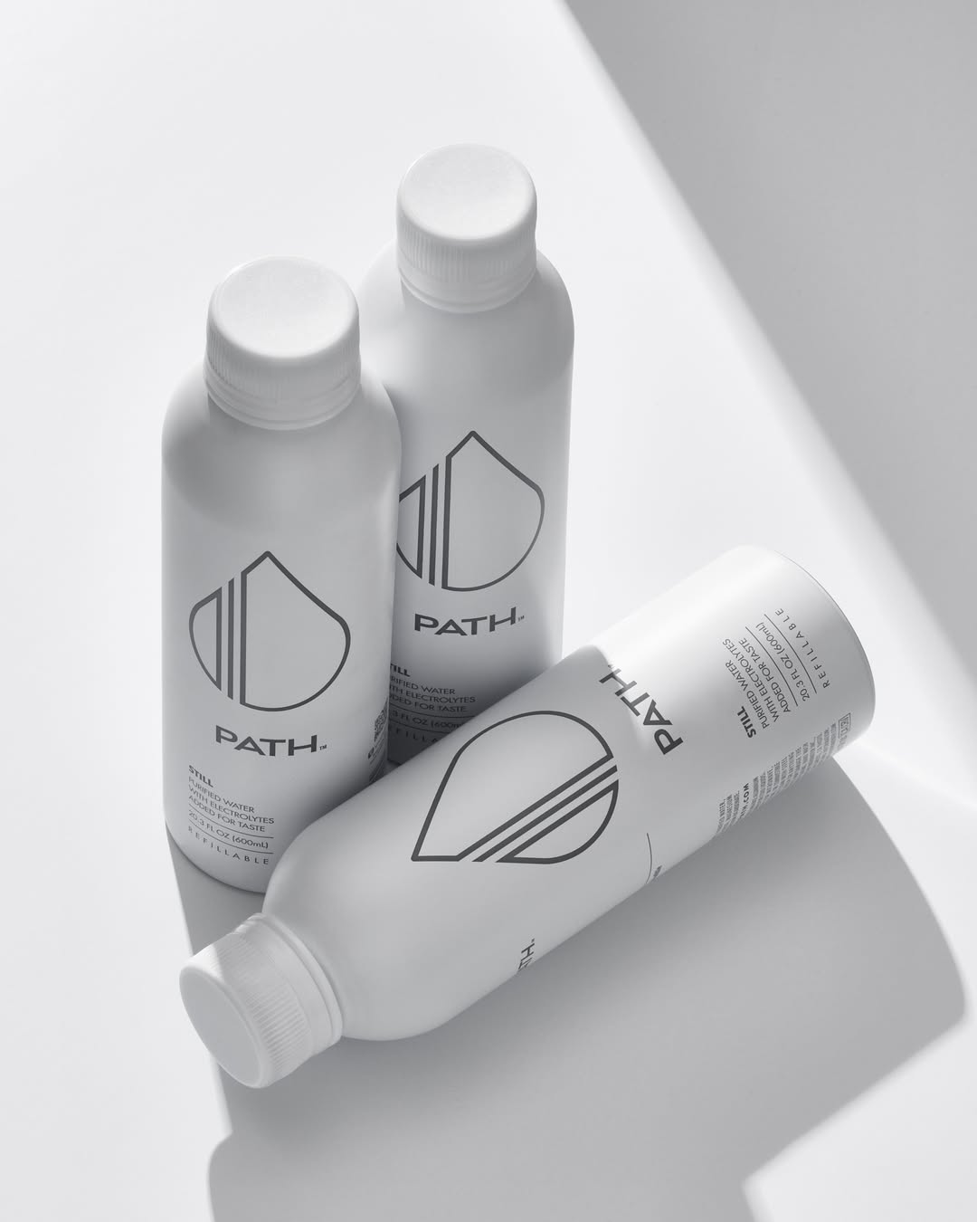 Top-down view of three PATH aluminum refillable bottles with visible logo, two upright and one on its side on a white surface