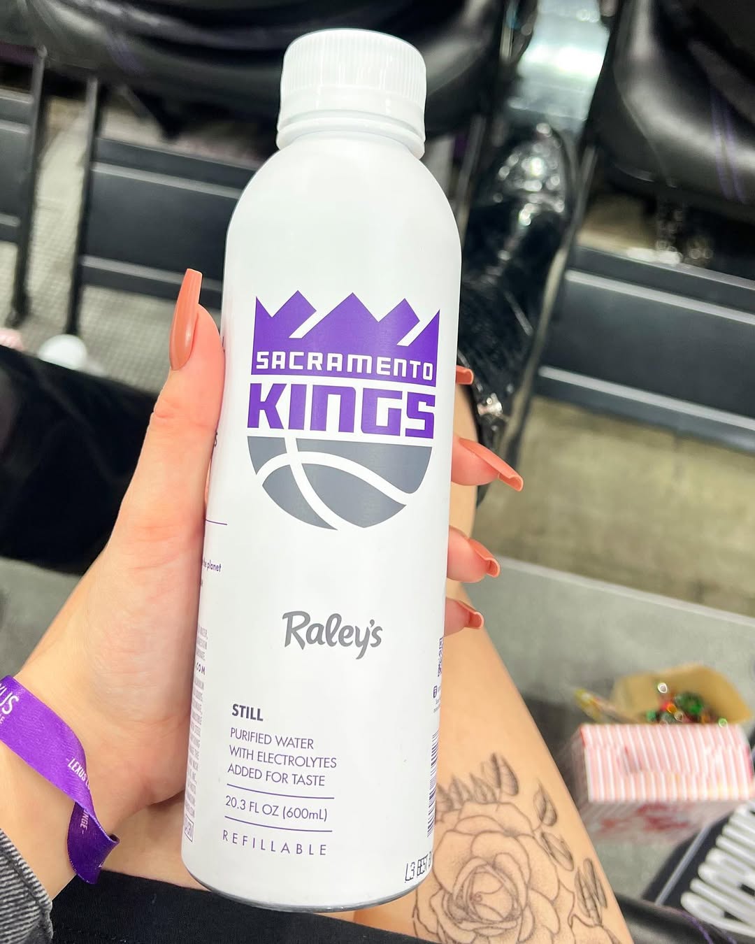 Front view of PATH refillable water bottle with purple Sacramento Kings logo held by a hand over arena seats