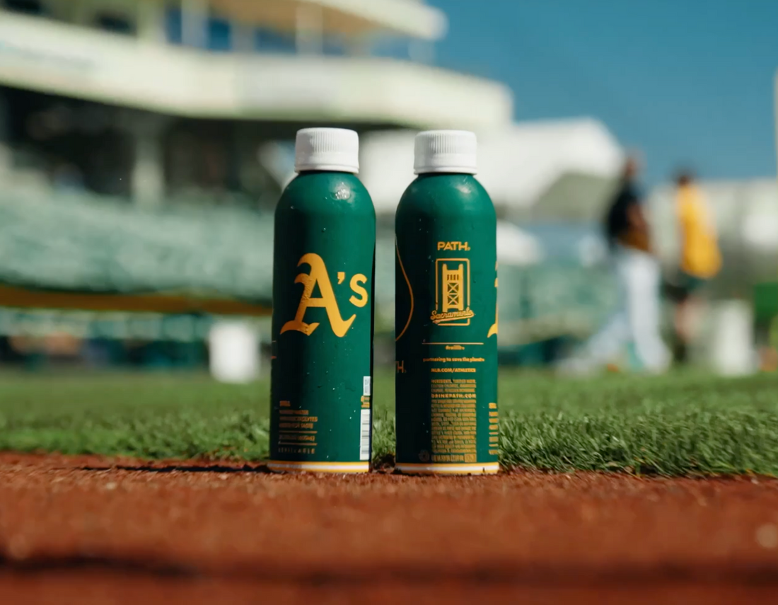 Front view of two green PATH refillable aluminum bottles showcasing Oakland A's logo and PATH co‑branding on a baseball field with blurred stands in the background