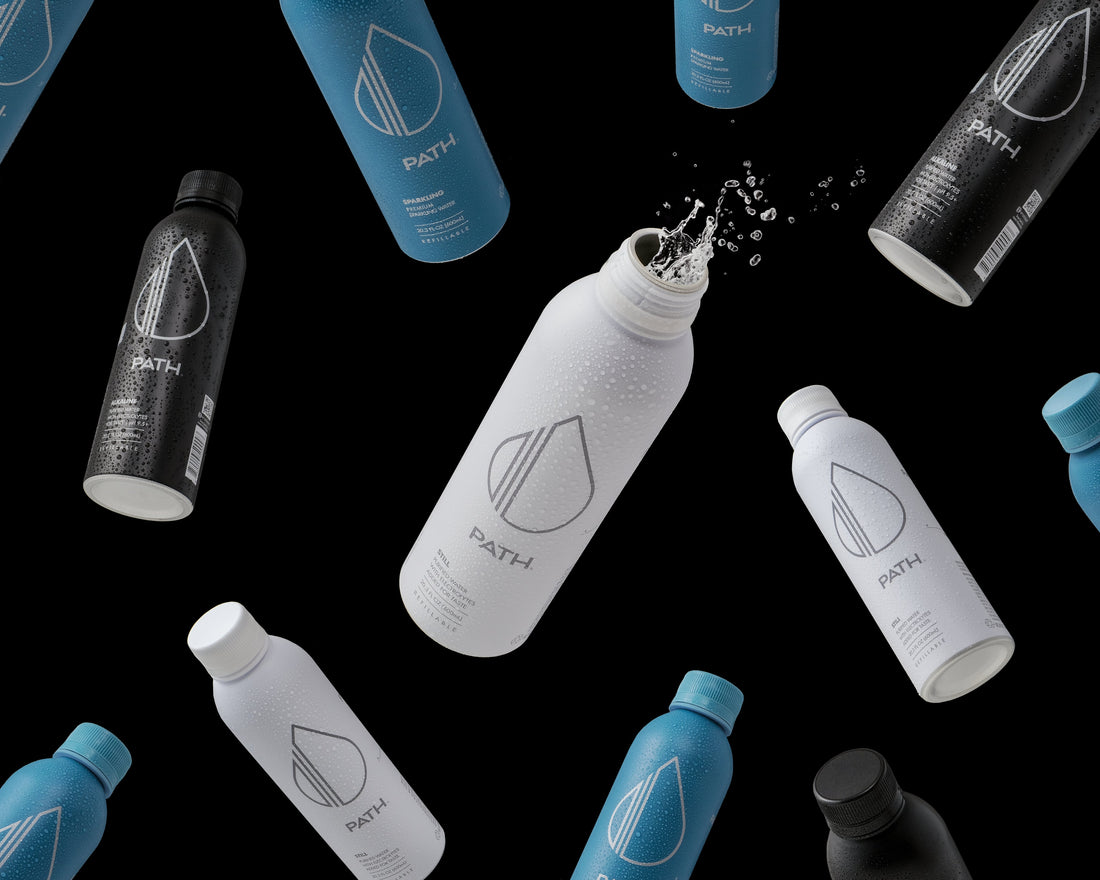 Angled view of PATH water bottles in white, blue, and black with logo, condensation, and a water splash on a black background