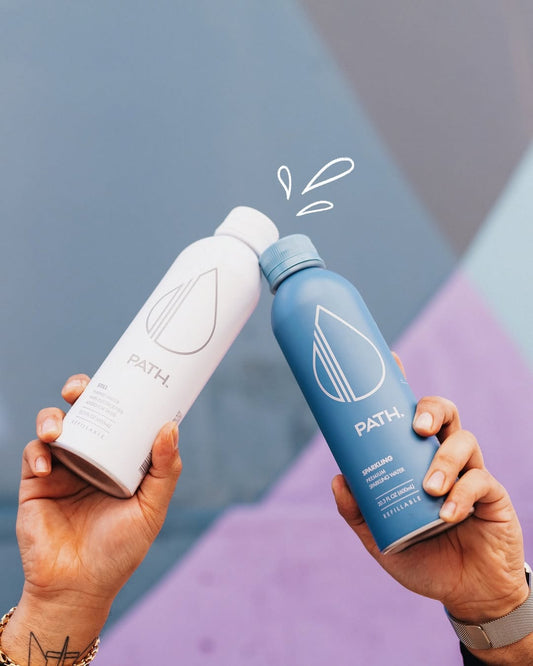 Two hands clinking a white PATH refillable aluminum bottle and a blue PATH refillable bottle against a pastel geometric background