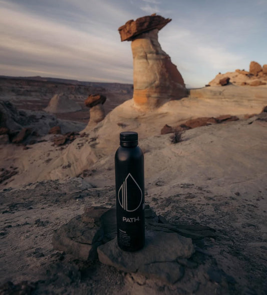 Front view of PATH aluminum water bottle showing white logo on matte black finish with desert rock formations in background