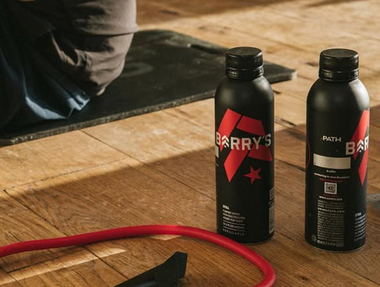Front and rear view of custom PATH water bottles showcasing black bottles with red and white Barry’s branding on a gym floor