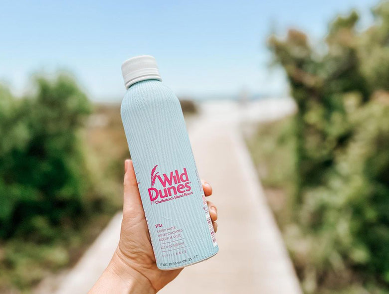Hand-held custom printed bottled water bottle showcasing Wild Dunes branding on an outdoor path