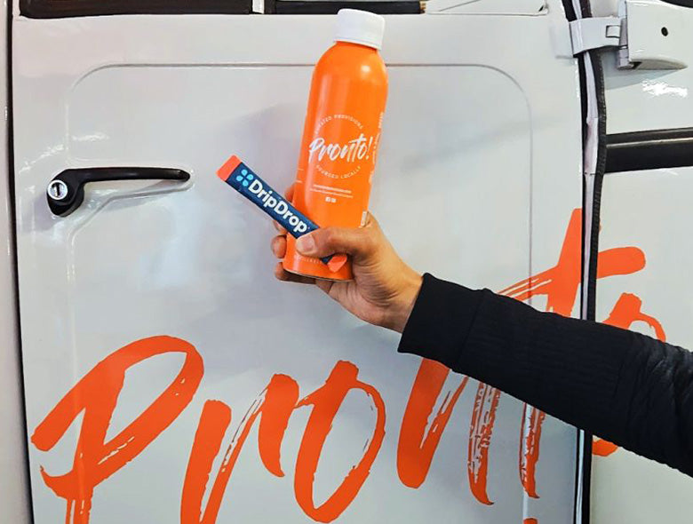 Front view of an orange custom-printed aluminum bottled water bottle with a white cap, held before a branded vehicle