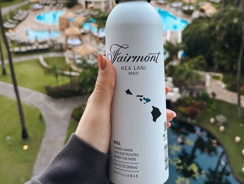 Close-up of a custom-printed aluminum water bottle with Fairmont Kea Lani Maui branding and a resort pool background