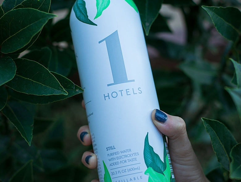 Close-up of a reusable bottled water bottle with a large 1 HOTELS design, held among leafy plants