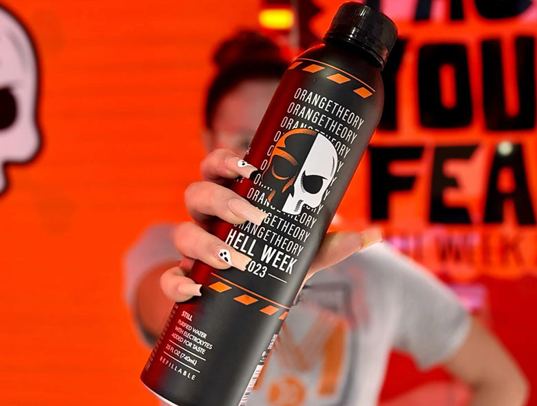 Angled view of an aluminum bottled water bottle showcasing custom Hell Week 2023 graphics, held in front of a person
