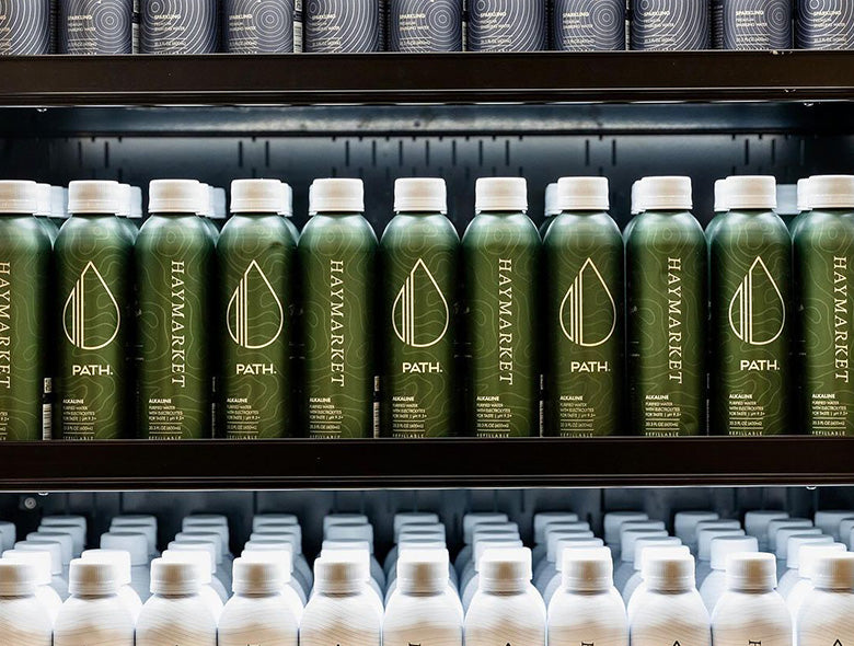 Front view of PATH aluminum bottled water bottles showcasing custom HAYMARKET labels on store shelves