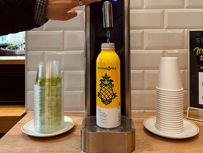 Custom-printed yellow bottle being filled at a dispenser beside stacks of cups